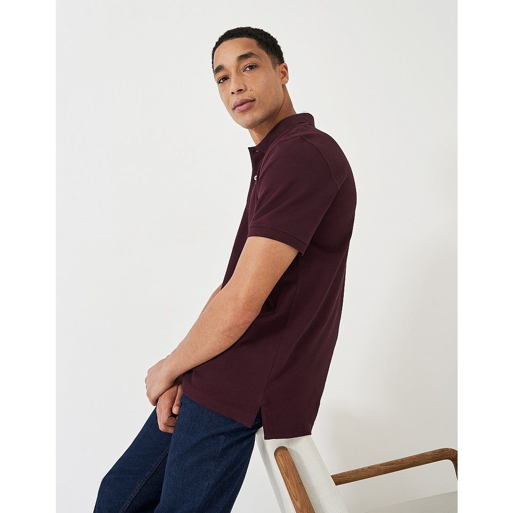 Side view of a man wearing a Crew Clothing short sleeve classic pique polo shirt in Heritage Burgundy with jeans