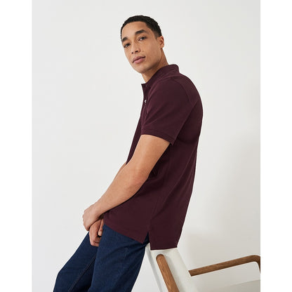Side view of a man wearing a Crew Clothing short sleeve classic pique polo shirt in Heritage Burgundy with jeans