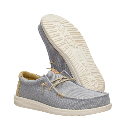 A pair of men's Dude Wally Braided lightweight canvas shoe in Flannel Grey / Olive Grey in a slip on style with laces, with one shoe upside down showing the outsole.