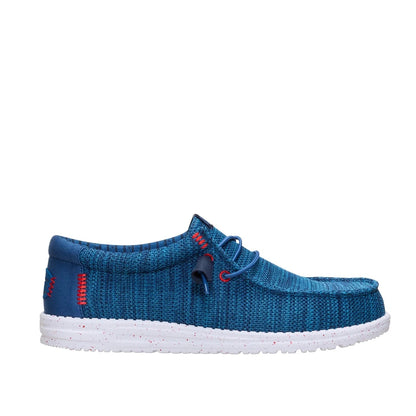 Side view of a men's Dude Wally Stretch Sox lightweight mesh shoe in Ensign Blue / Multi, with elastic laces a white speckled sole and red stitching accents.