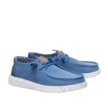 A pair of women's Dude Wendy Chambray Grid shoe in Ensign Blue, featuring matching blue elastic laces, speckled white soles and brown Hey Dude logo on the tongues.