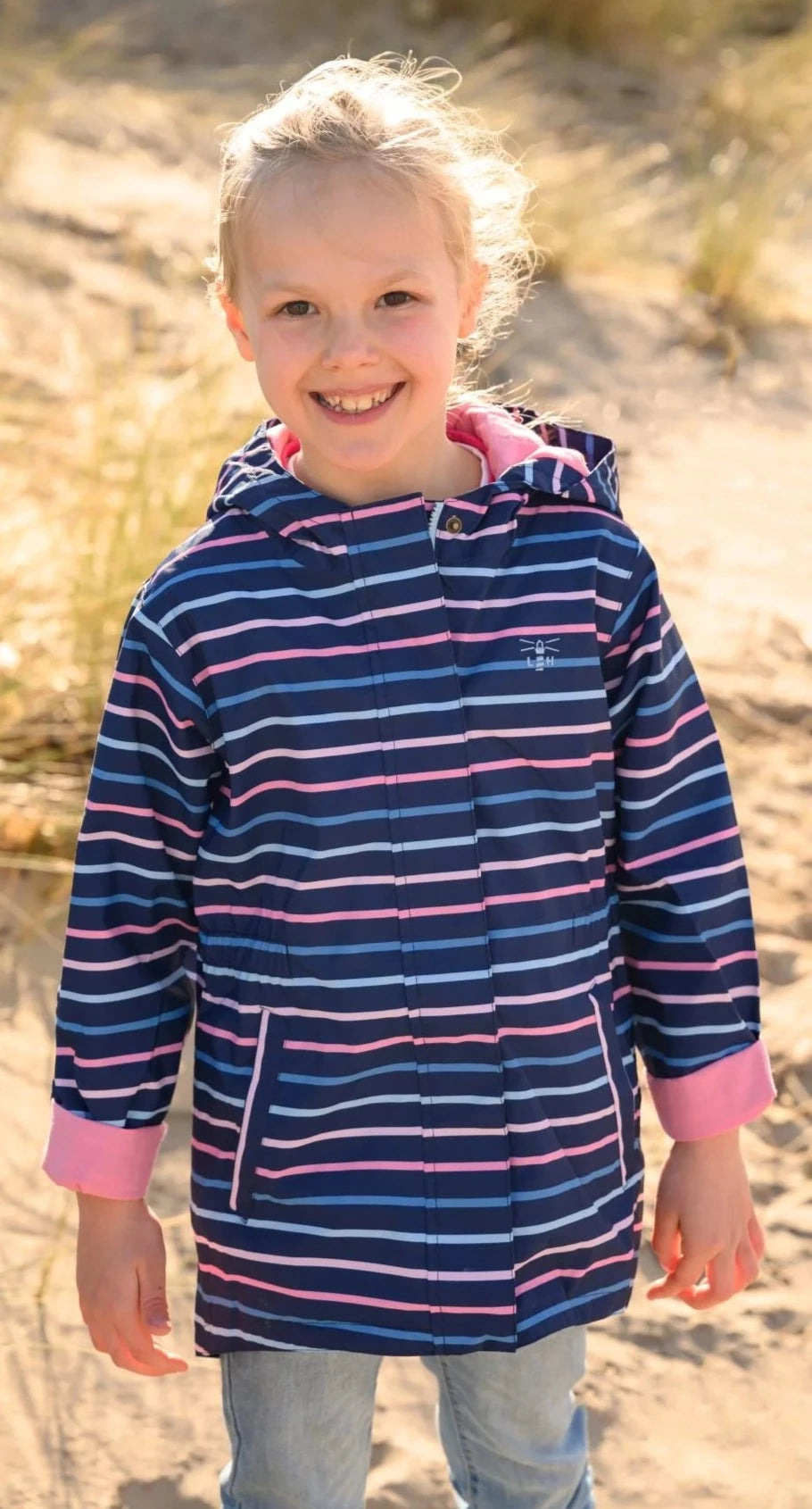 Child wearing a Lighthouse Charlotte waterproof jacket in navy with a pink and blue stripe pattern outdoors.