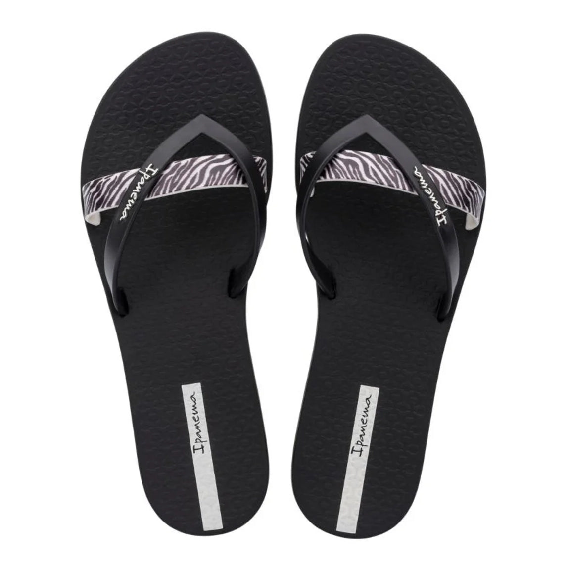 Top view of a pair of women's Ipanema Kirei flip flops, a three strap toepost design in black with a contrasting zebra print strap and textured footbed.