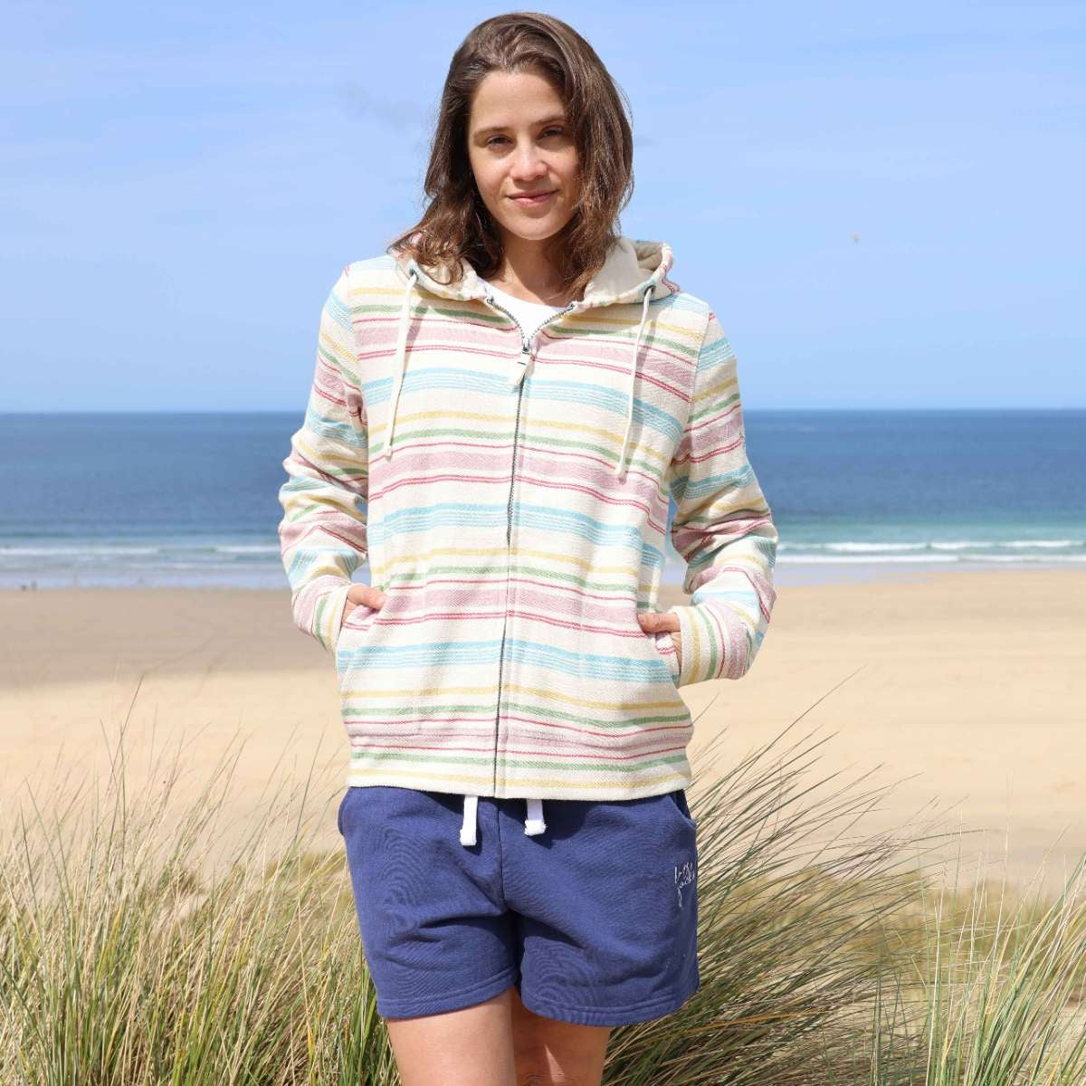 Front view of a woman wearing a Lazy Jacks LJ302 full zip hoodie in multicoloured pastel stripes with tummy pockets and blue shorts