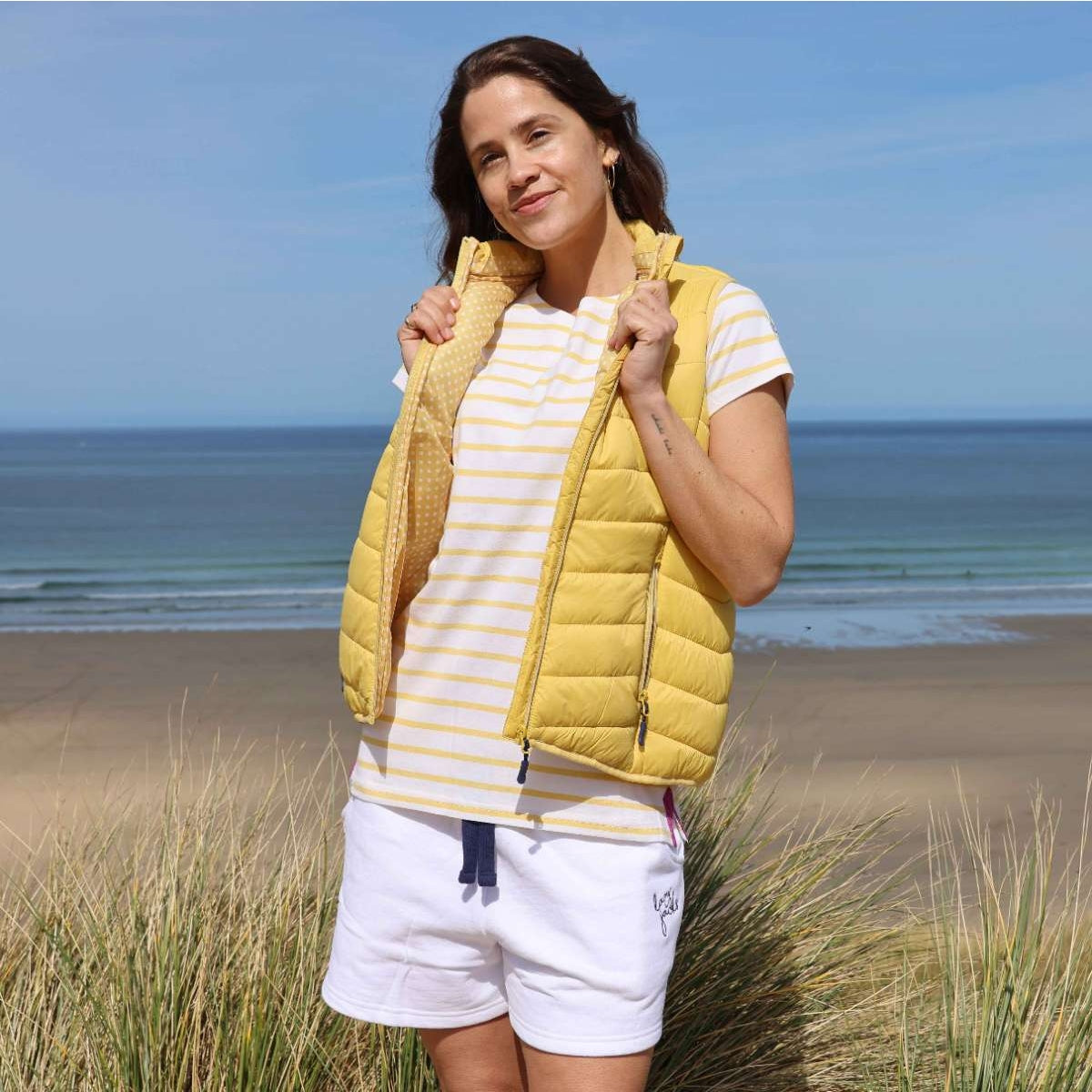 Woman wearing a Lazy Jacks lemon yellow GL2 lightweight padded gilet unzipped, with a dotty lining.