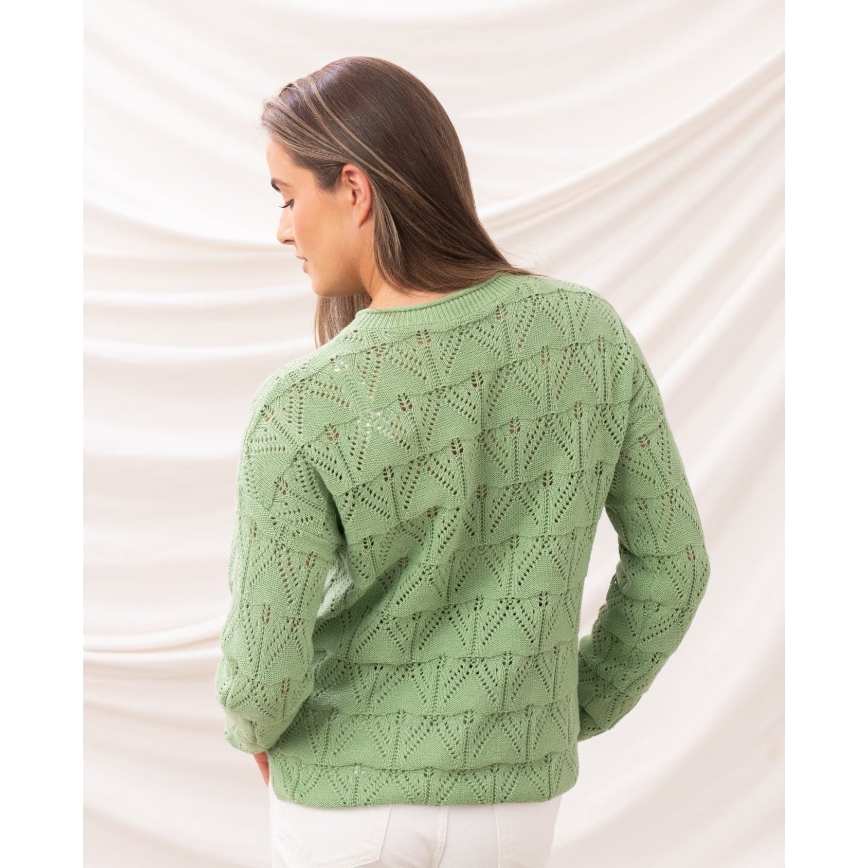 Back view of a woman wearing a Lighthouse Eden knitted jumper in Soft Sage Green with a geometric pointelle knit pattern.