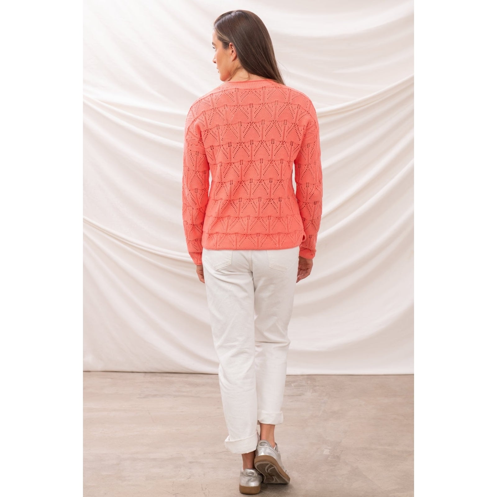 Back view of a woman wearing a Lighthouse Eden jumper in a bright Sugar Coral colour with pointelle style knit.