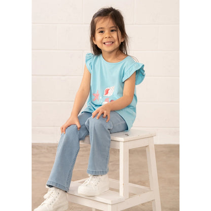 Child sitting on a stool wearing a light blue Lighthouse top and jeans with a white background