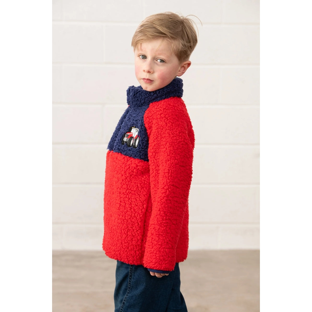 Side view of a child wearing a red and navy Lighthouse Caden fleece jumper against a white wall