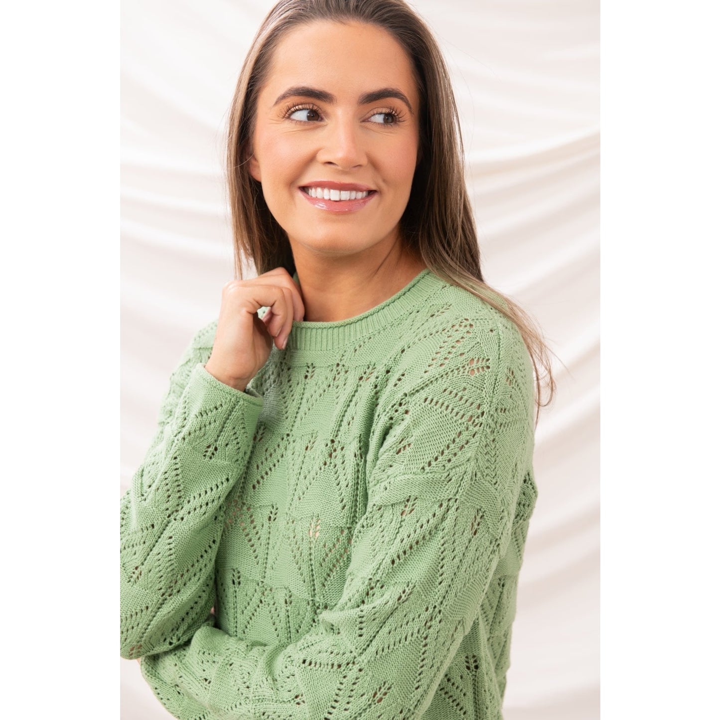 Close-up side view of a woman wearing a Lighthouse Eden knitted jumper in Soft Sage Green with a geometric pointelle knit pattern.