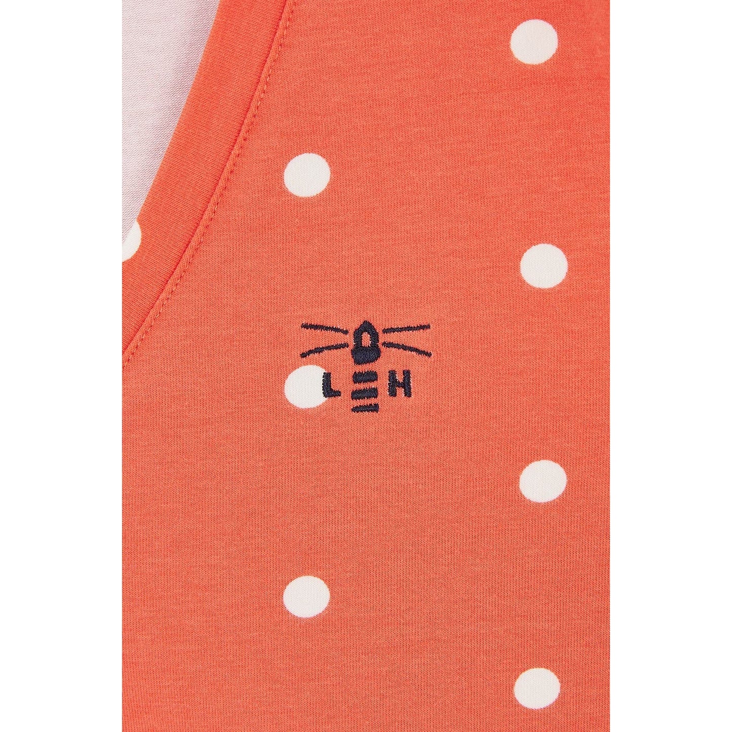 Close-up view of a Lighthouse short sleeve Ariana v-neck t-shirt in coral with a white dot pattern and a small Lighthouse logo.