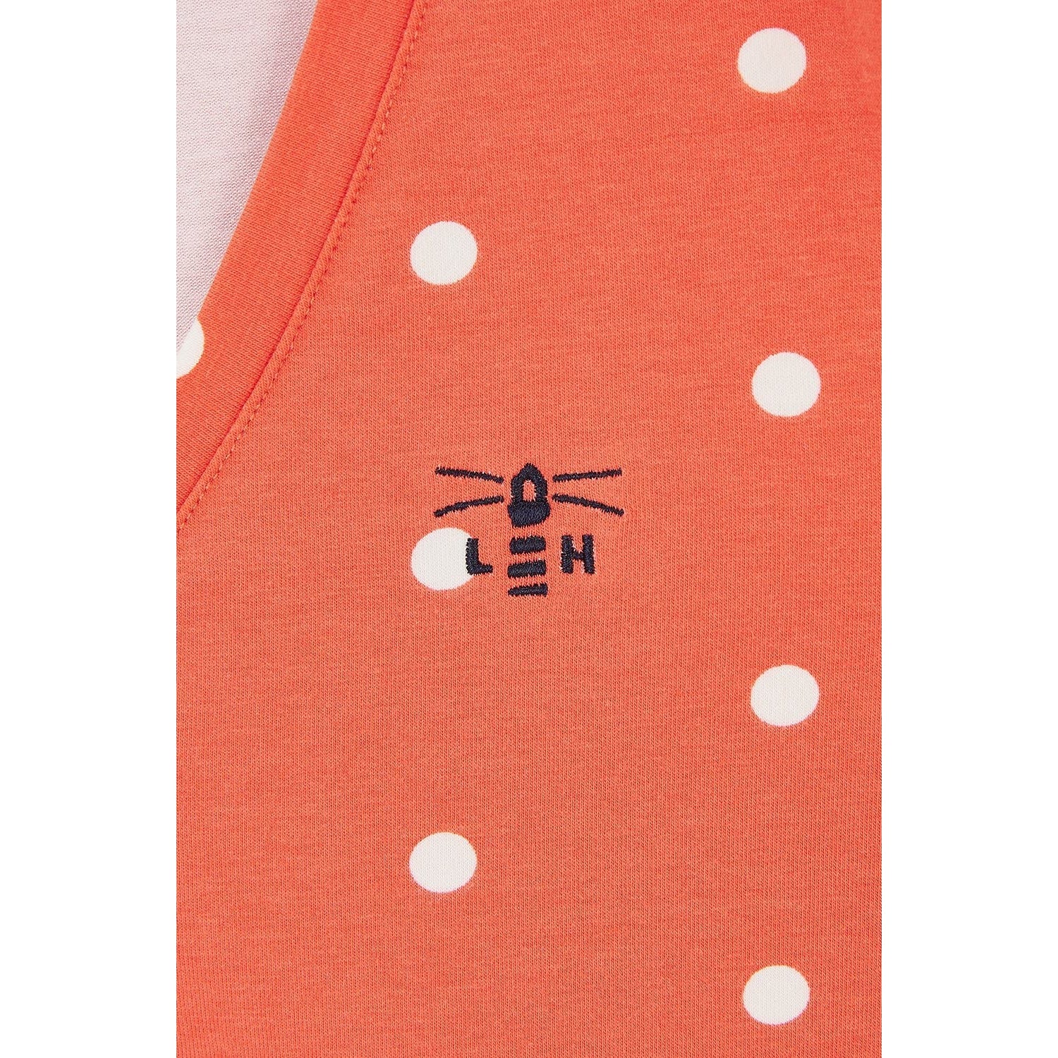Close-up view of a Lighthouse short sleeve Ariana v-neck t-shirt in coral with a white dot pattern and a small Lighthouse logo.