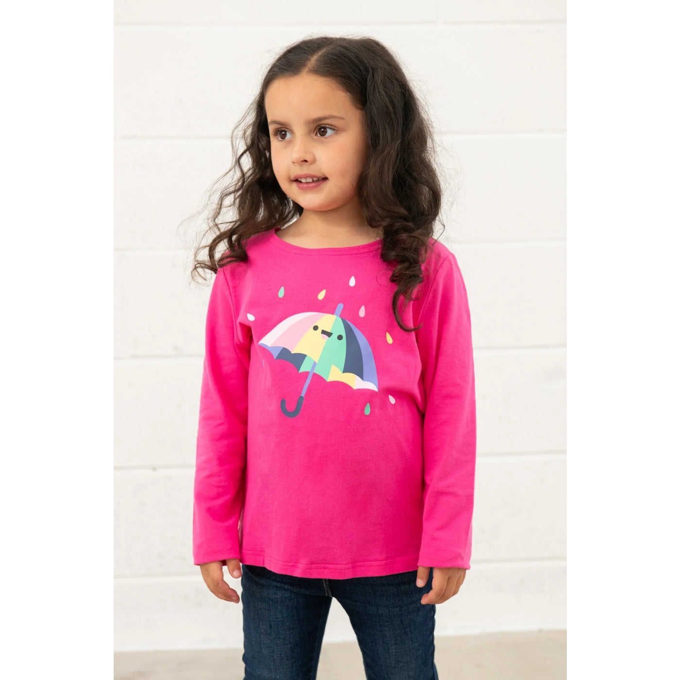 Young girl wearing a Lighthouse Causeway pink long-sleeve t-shirt with a colourful umbrella print on a white background