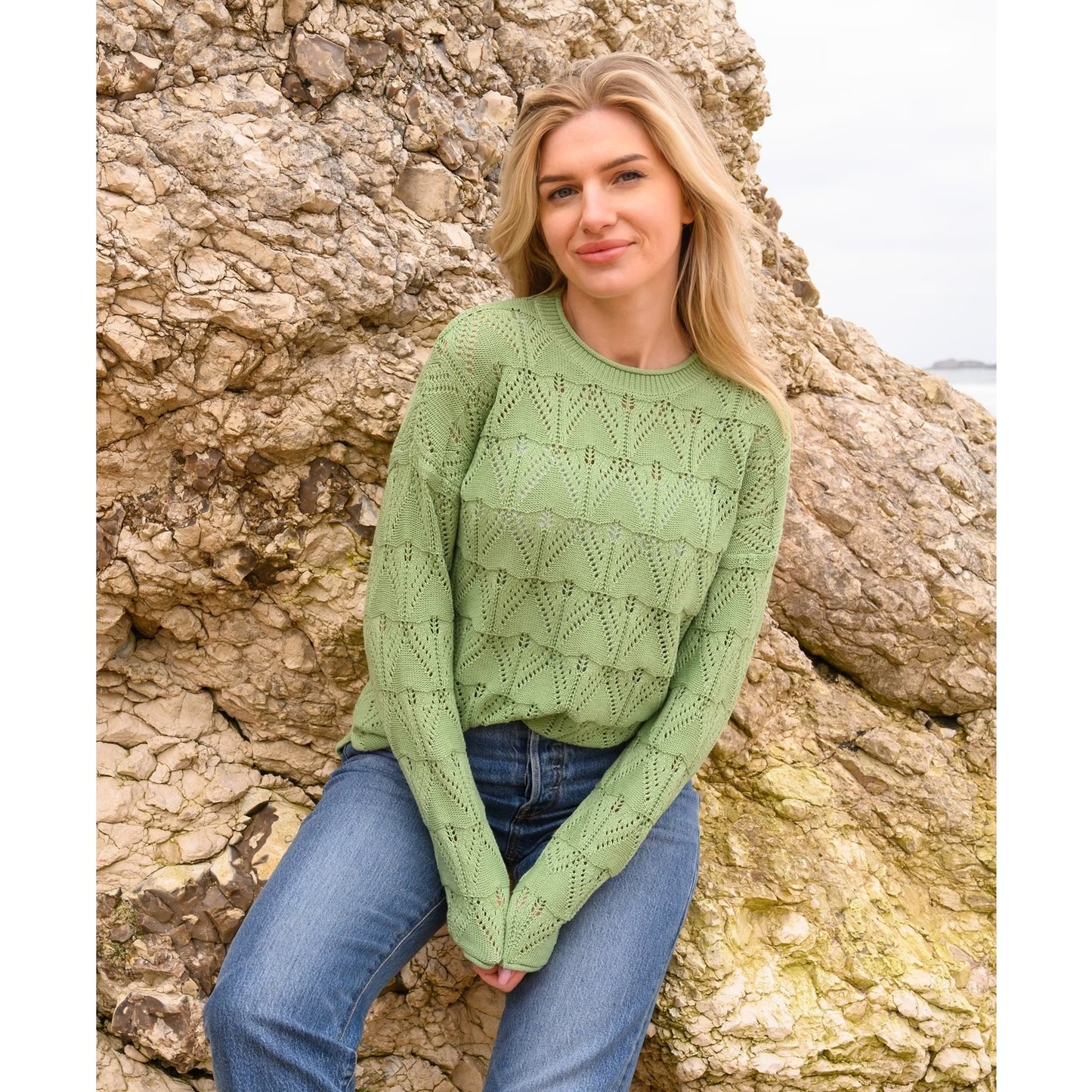 Outdoor view of a woman wearing a Lighthouse Eden knitted jumper in Soft Sage Green with a geometric pointelle knit pattern.
