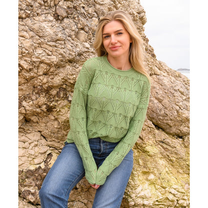 Outdoor view of a woman wearing a Lighthouse Eden knitted jumper in Soft Sage Green with a geometric pointelle knit pattern.