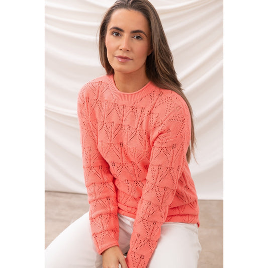 Front view of a woman wearing a Lighthouse Eden jumper in a bright Sugar Coral colour with pointelle style knit with white trousers.