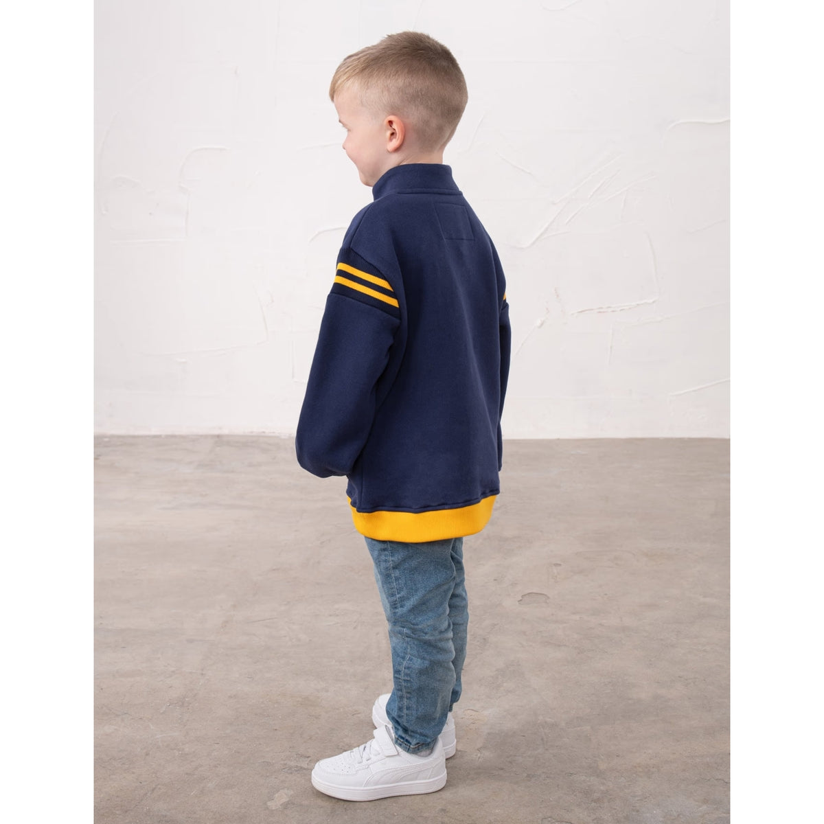 Back view of a boy wearing a Lighthouse Jonah 1/4 zip sweatshirt in navy with yellow trim and a JCB applique sewn on the chest.
