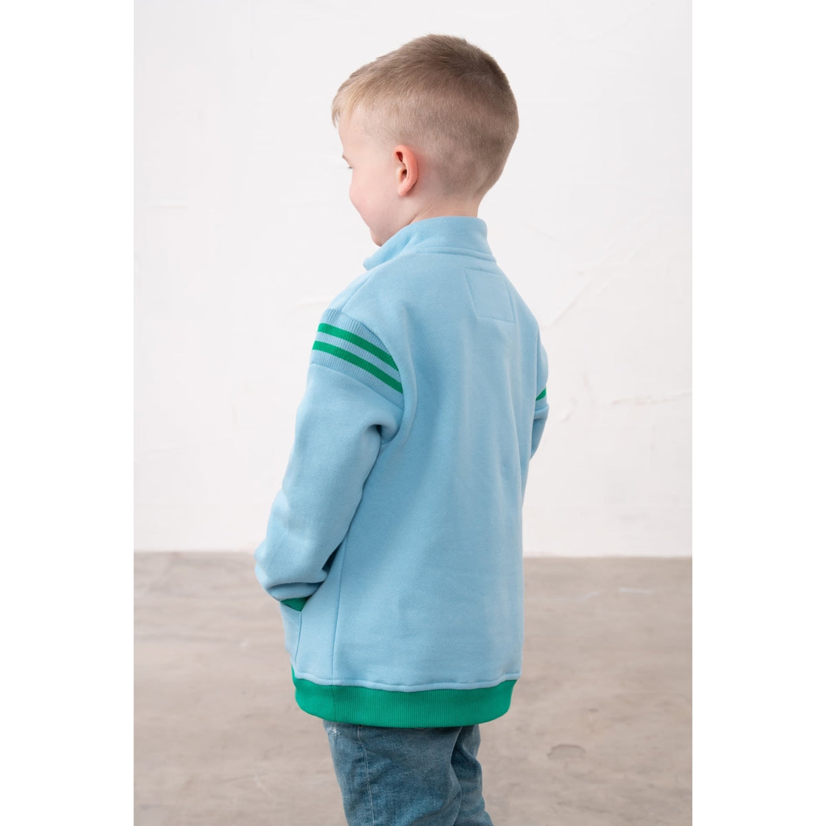 Back view of a child wearing a Lighthouse Jonah zip neck sweatshirt in sky blue with green trim and tractor applique on the chest.