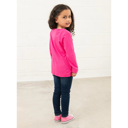 Back view of a young girl wearing a Lighthouse bright pink long-sleeve Causeway tee and dark blue jeans against a white background