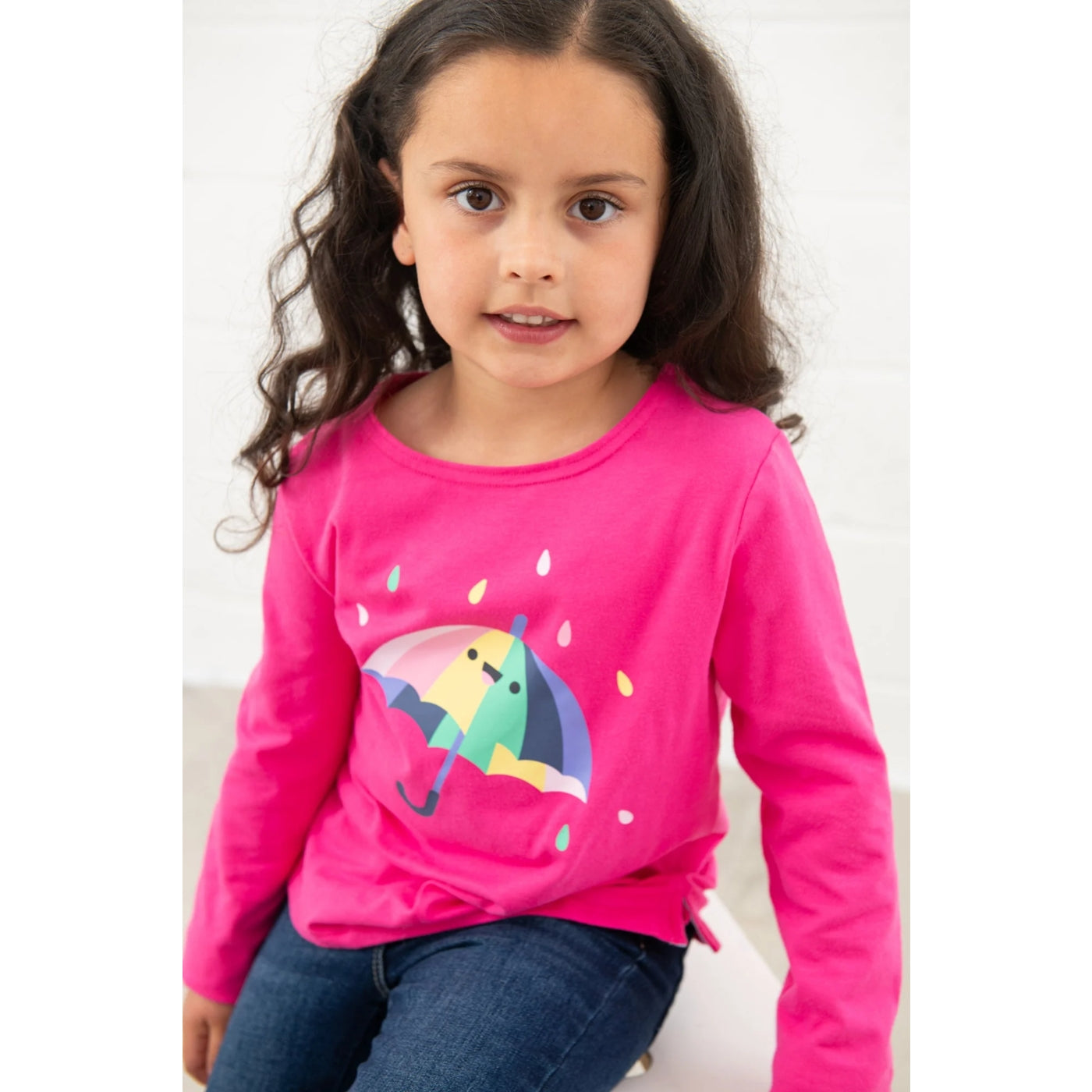 Girl wearing a pink long-sleeve Lighthouse Causeway t-shirt with a colourful umbrella print on a white background