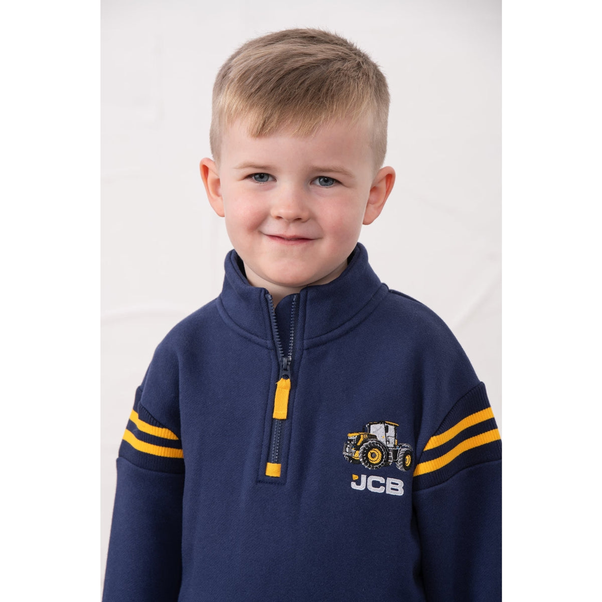 Close-up view of a boy wearing a Lighthouse Jonah 1/4 zip sweatshirt in navy with yellow trim and a JCB applique sewn on the chest.