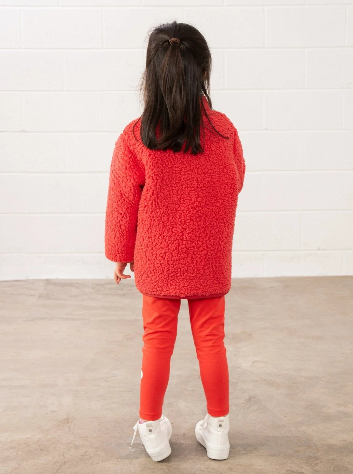 Child wearing Lighthouse kids coral leggings paired with a coral fuzzy jacket and white sneakers