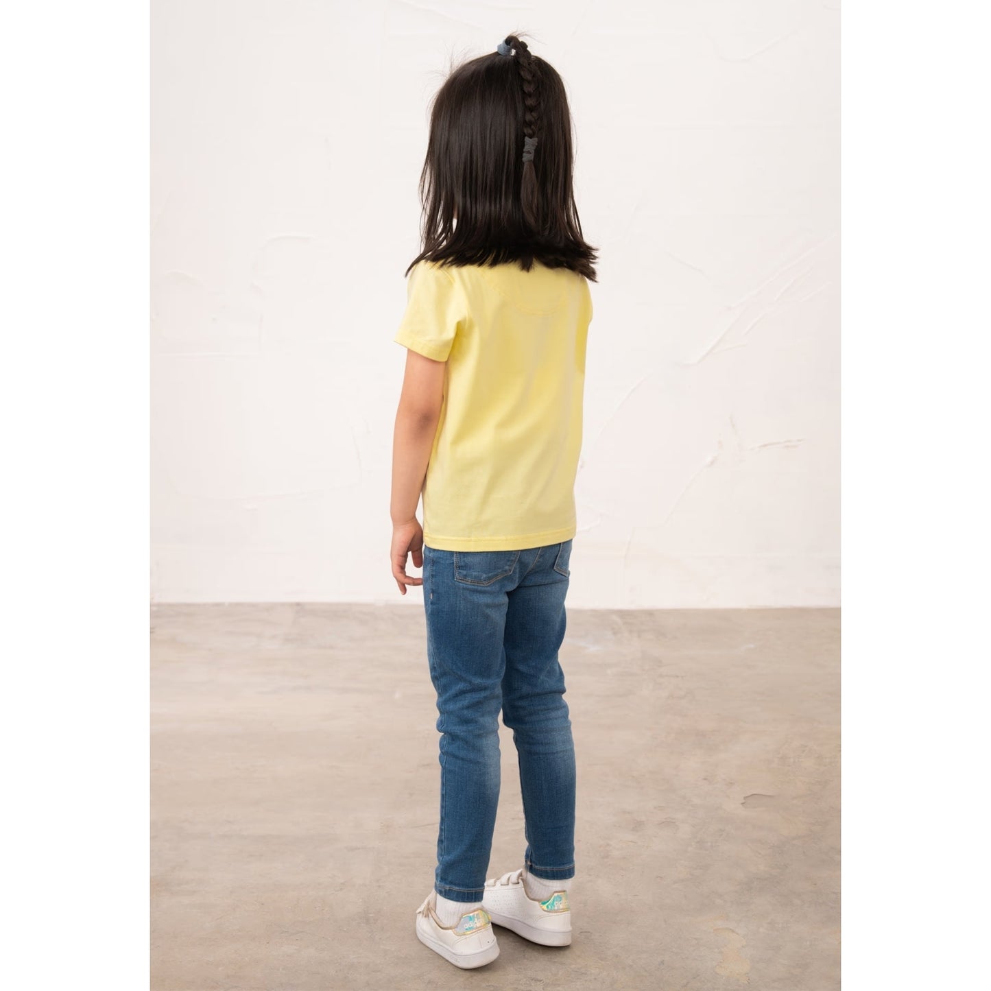 Back view of a girl wearing a kids Lighthouse short sleeve Causeway t-shirt in lemon yellow, featuring a heart shape ballerina print on the front.