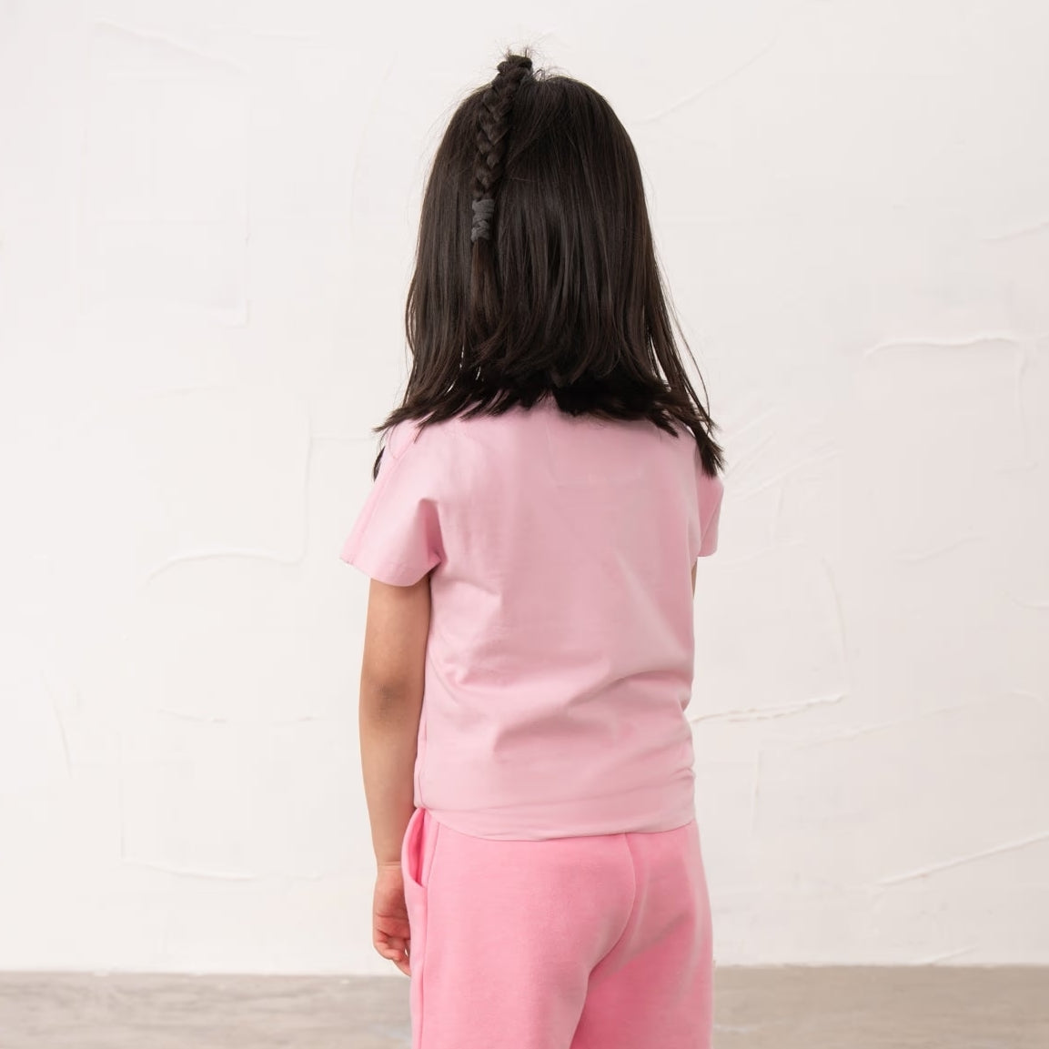 Back view of a girl wearing a Lighthouse Causeway short sleeve tee in pink with a tie hem and embroidered bow on the front.