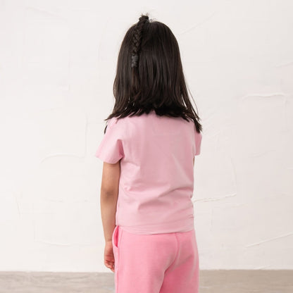 Back view of a girl wearing a Lighthouse Causeway short sleeve tee in pink with a tie hem and embroidered bow on the front.