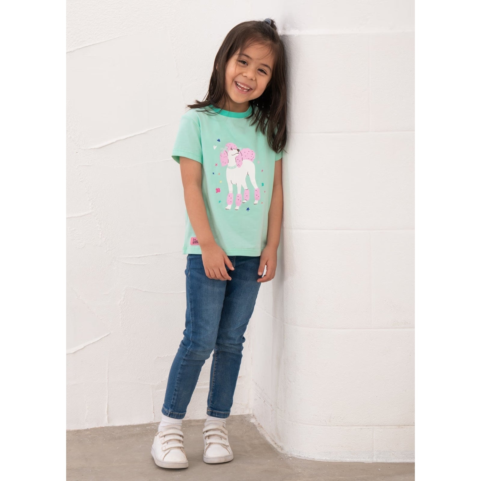 Front view of a girl wearing a kids Lighthouse short sleeve Causeway t-shirt in mint green, featuring a white and pink poodle dog print on the front.