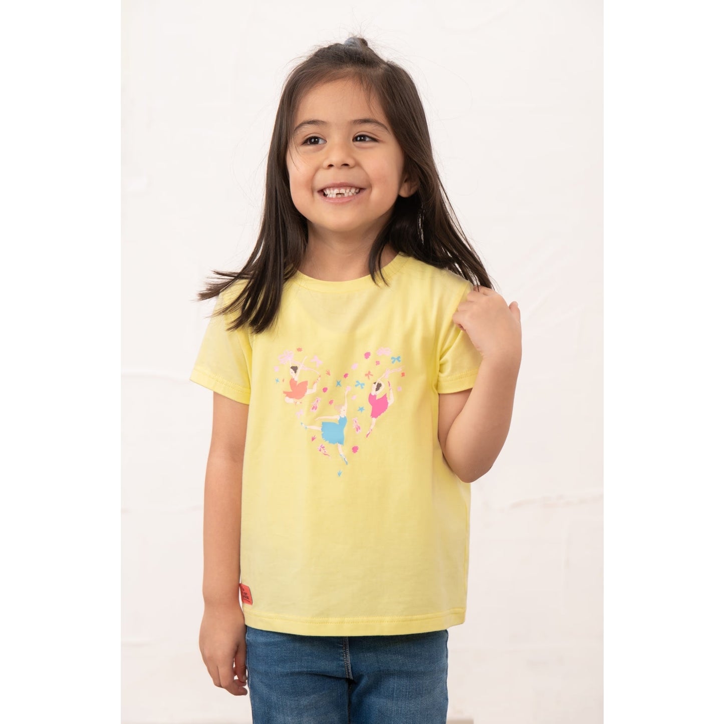 Front view of a girl wearing a kids Lighthouse short sleeve Causeway t-shirt in lemon yellow, featuring a heart shape ballerina print on the front.