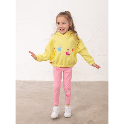 Girl wearing a pair of Lighthouse kids Mollie leggings in Fluro Pink with a bow, heart and flower print on one leg with yellow hoodie.