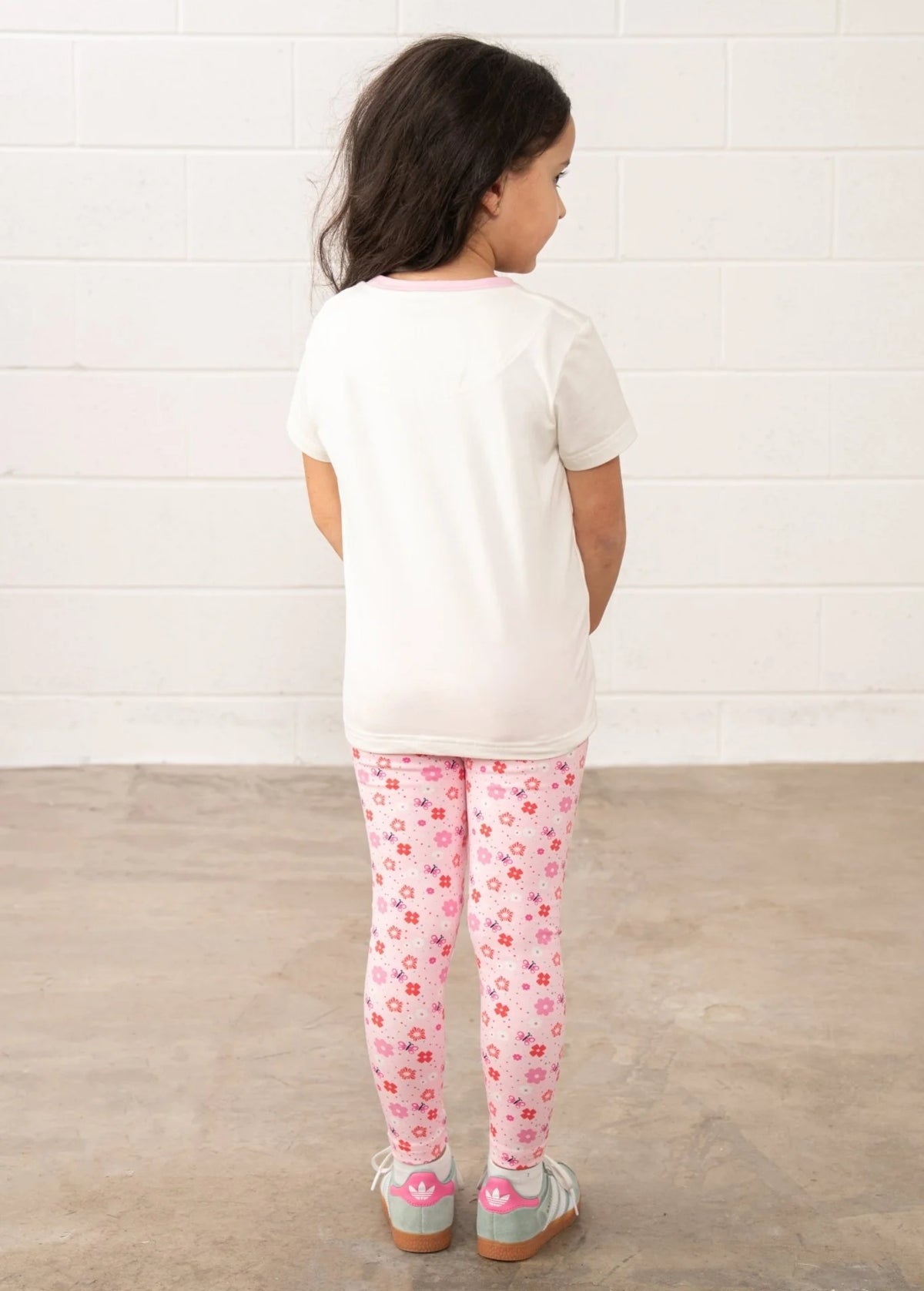 Back view of a child wearing Lighthouse kids Princess Tee white t-shirt with pink trim and floral leggings