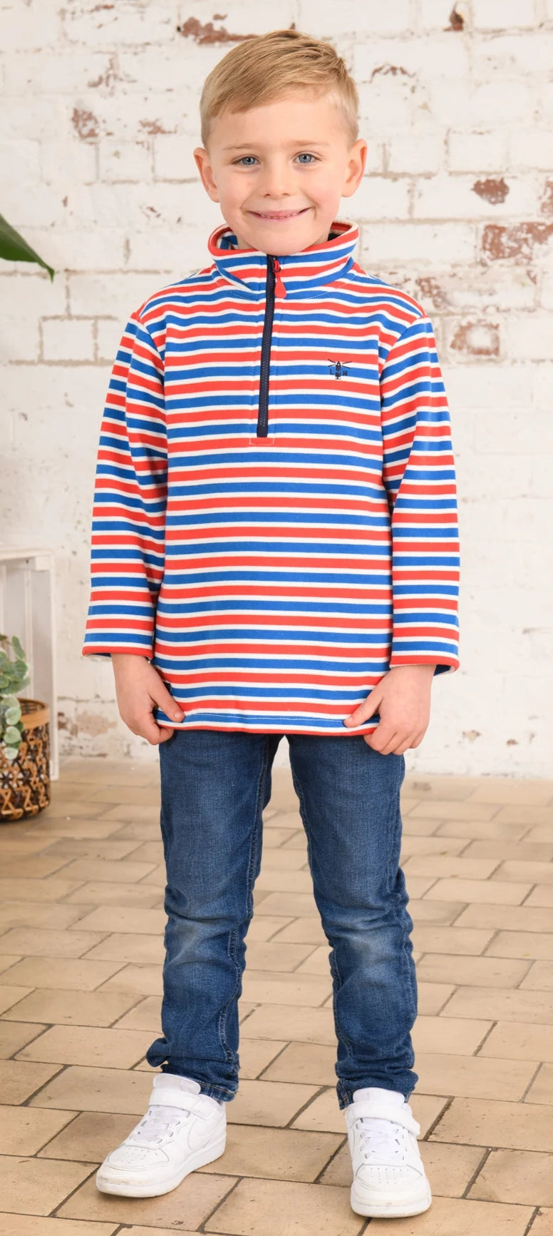 A boy wearing a Lighthouse Riley 1/4 zip sweatshirt in a red, blue and white stripe patter.