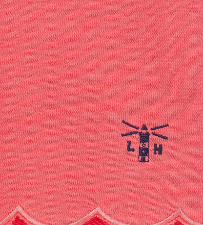 Close-up of coral fabric with scalloped edge and lighthouse logo on Lighthouse kids shorts coral