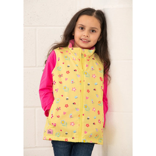 Front view of a Lighthouse kids yellow floral gilet worn by a girl with pink long sleeve shirt and dark jeans