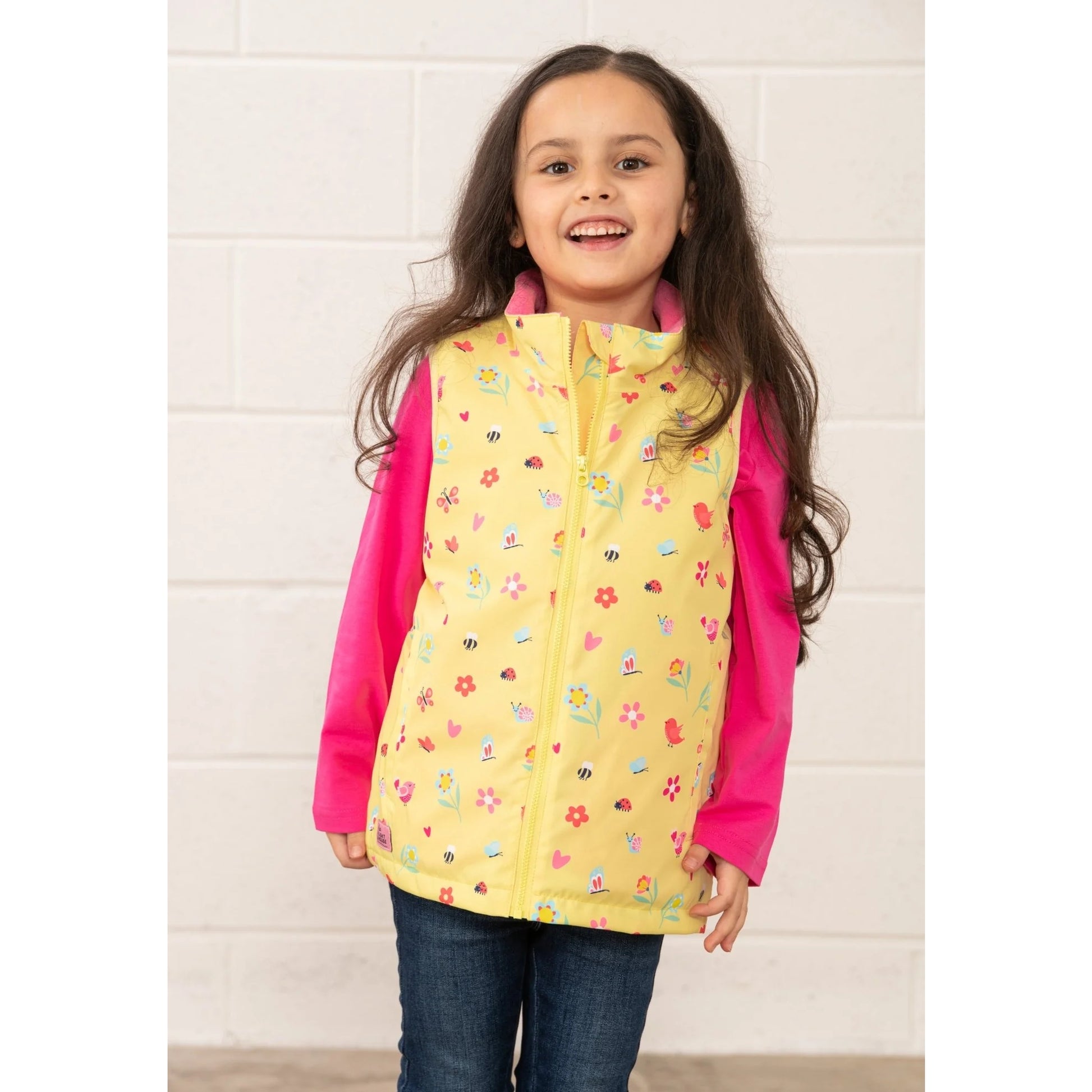 Lighthouse kids yellow floral gilet worn by smiling girl with pink long sleeve shirt and jeans