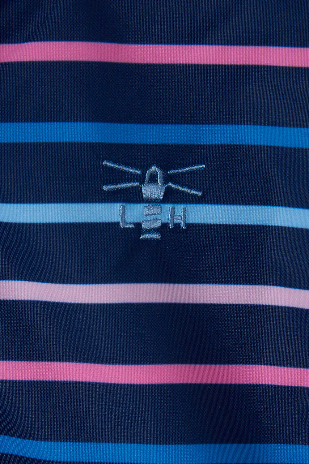 Close up of a Lighthouse kids Charlotte  waterproof coat logo on navy, pink and blue stripe fabric