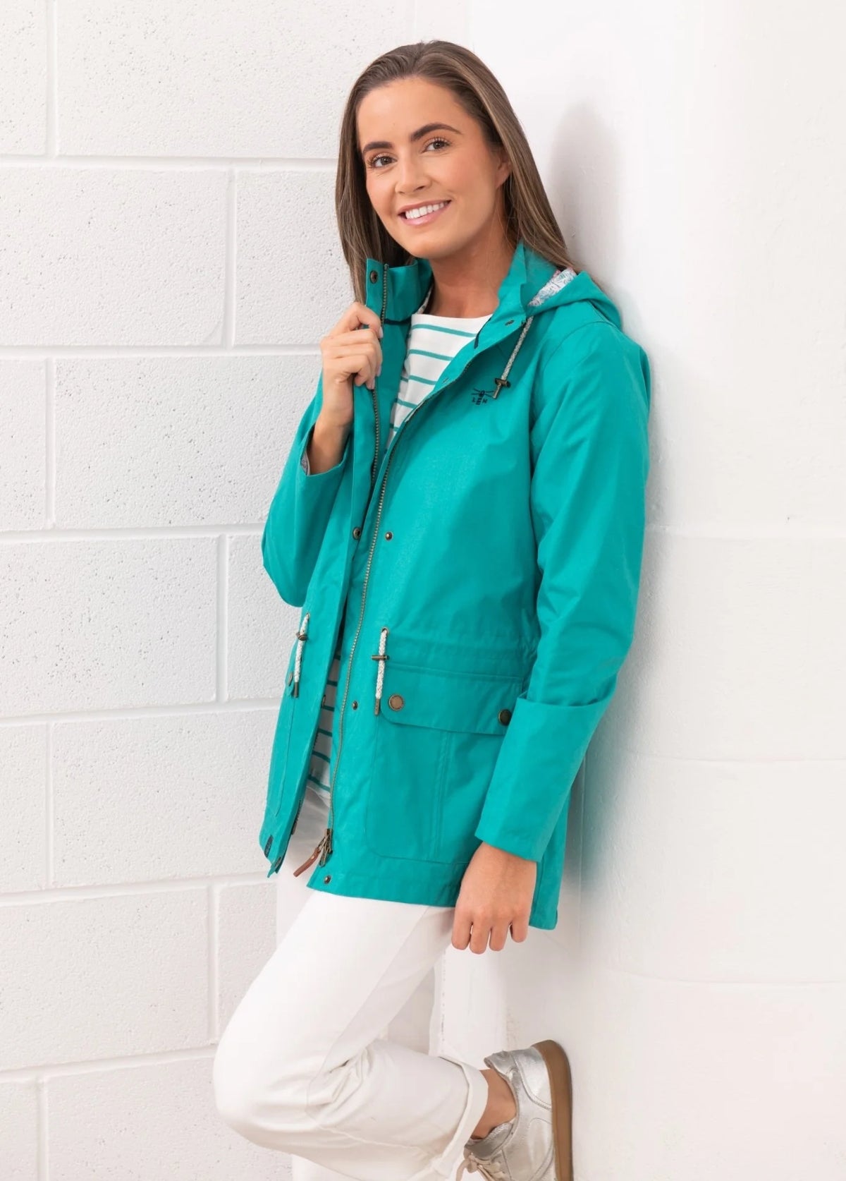 Lighthouse teal womens waterproof jacket worn by smiling woman leaning against white wall