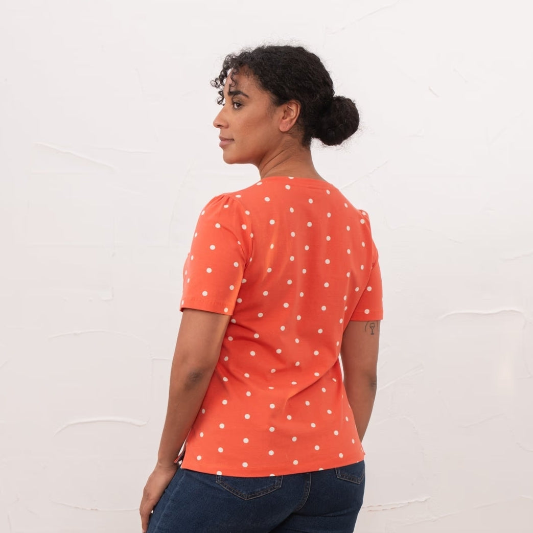 Back view of a woman wearing a Lighthouse short sleeve Ariana v-neck t-shirt in coral with a white dot pattern.