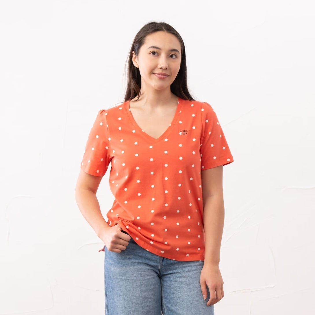 A woman wearing a Lighthouse short sleeve Ariana v-neck t-shirt in coral with a white dot pattern.