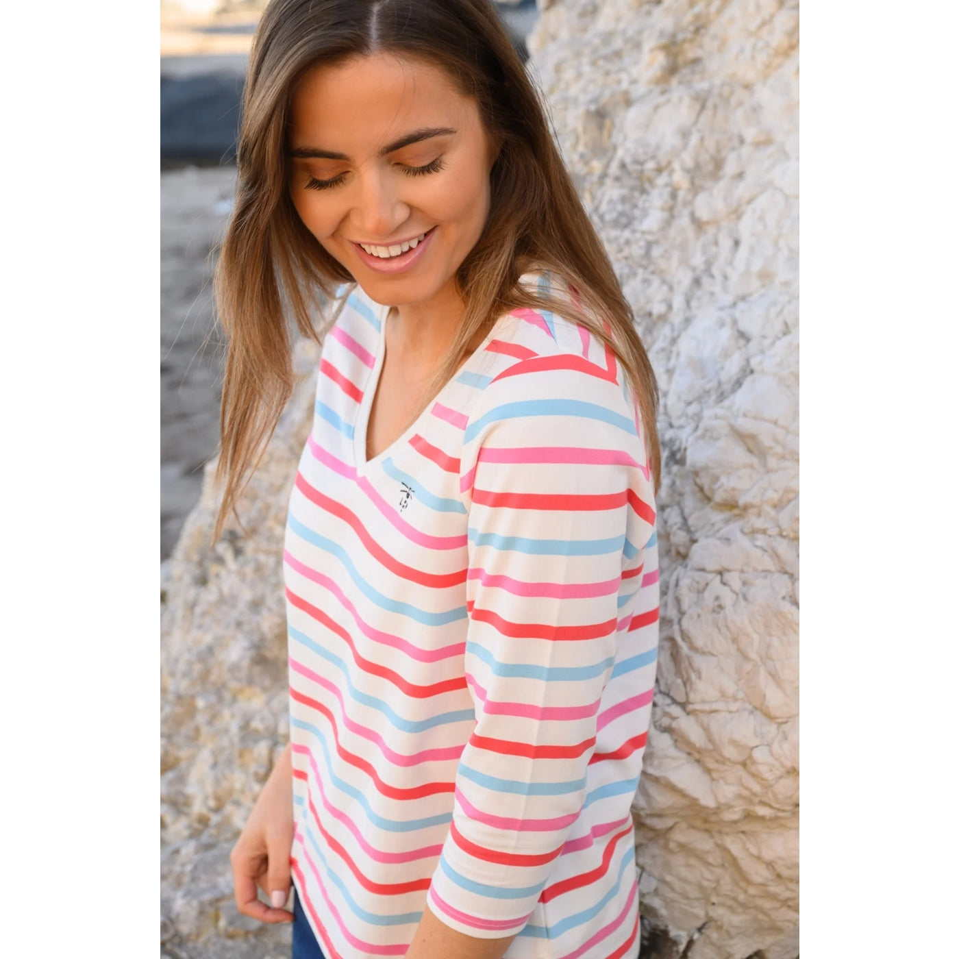 Woman wearing a colourful stripe Lighthouse Ariana top standing against a textured wall.