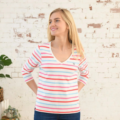 Front view of a woman wearing a Lighthouse Ariana v-neck top in Watermelon Pink Stripe standing against a brick wall.