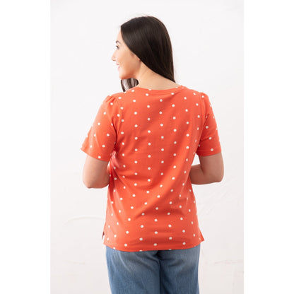 Back view of a woman wearing a Lighthouse short sleeve Ariana v-neck t-shirt in coral with a white dot pattern and blue jeans.