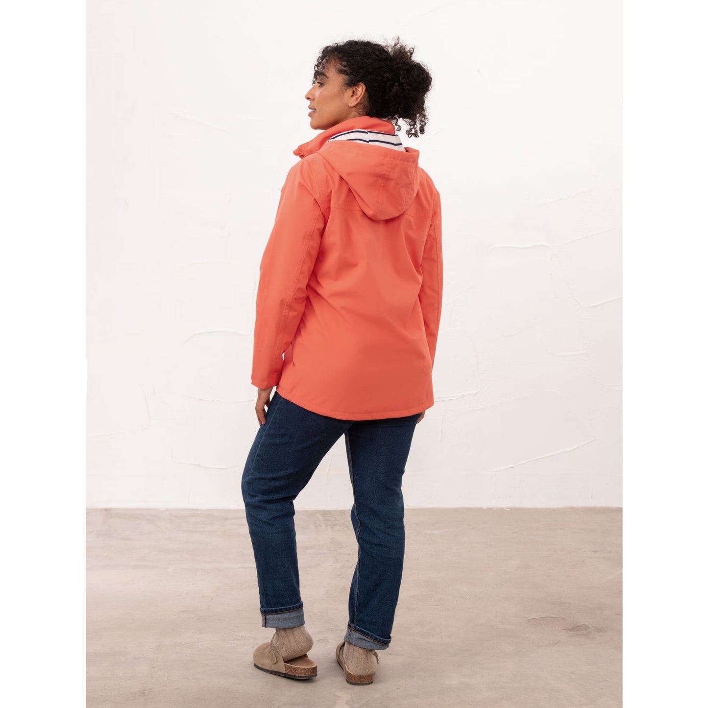 Back view of a womens Beachcomber II waterproof jacket in Coral with blue jeans.
