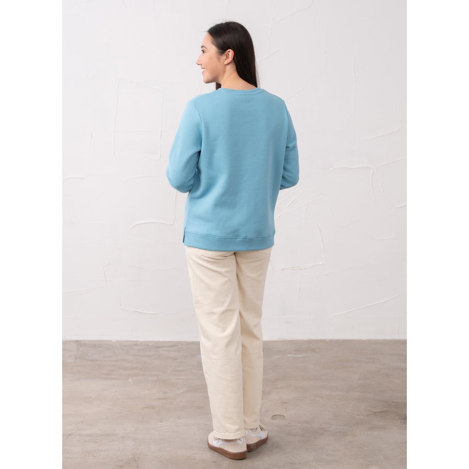 Back view of a woman wearing a Lighthouse Seaside crew neck sweatshirt in Blue with cream trousers.