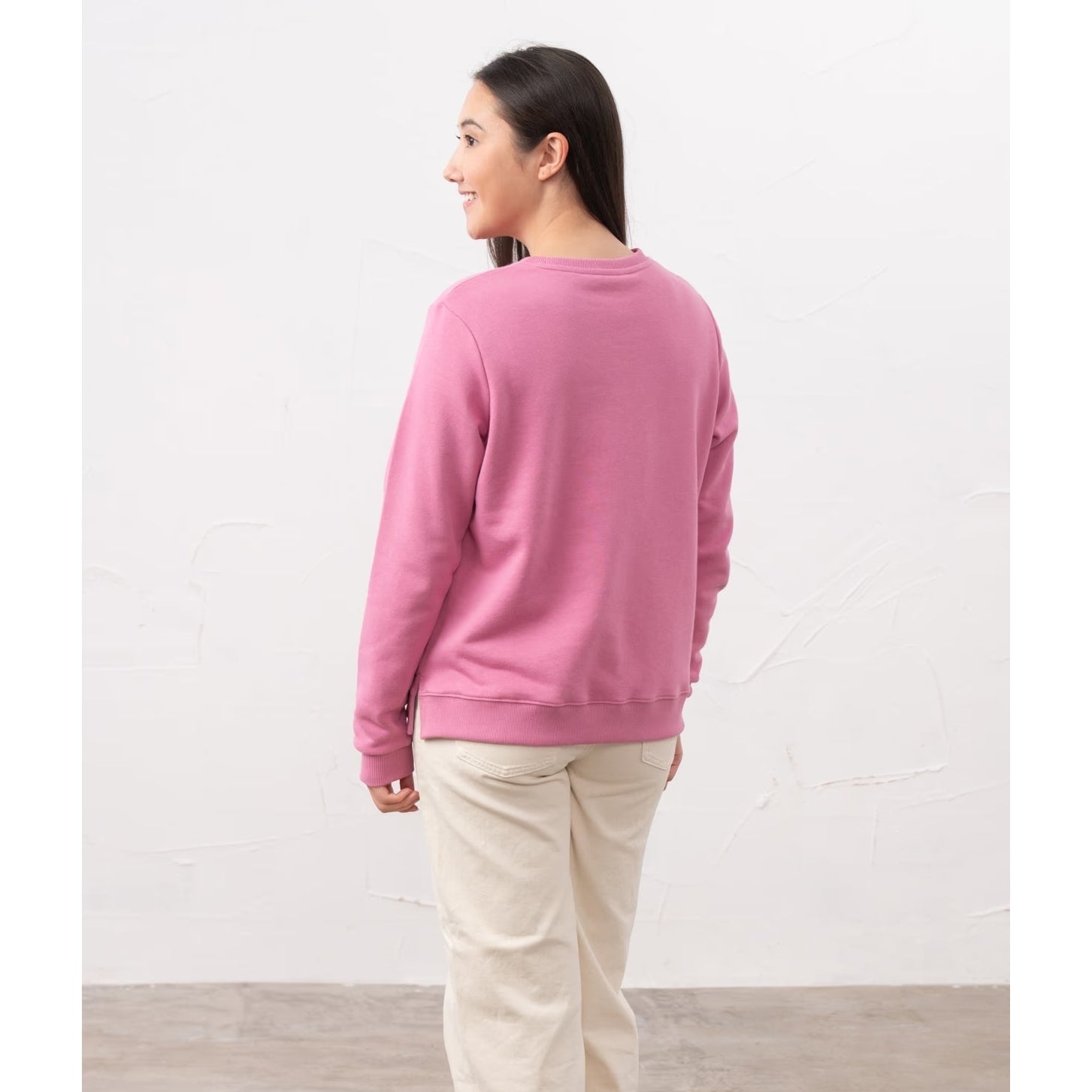 Back view of a woman wearing a Lighthouse Seaside crew neck sweatshirt in Pink with cream trousers.