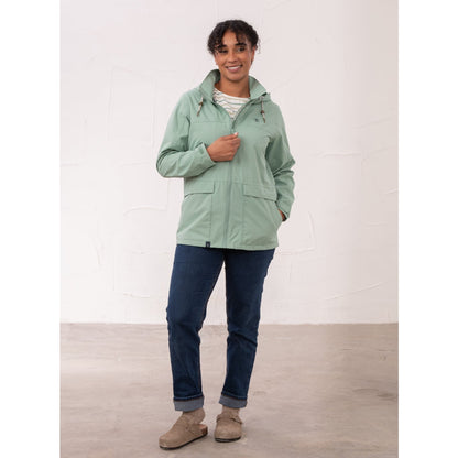 A woman wearing a Lighthouse waterproof Beachcomber II waterproof jacket in Basil green with blue jeans.
