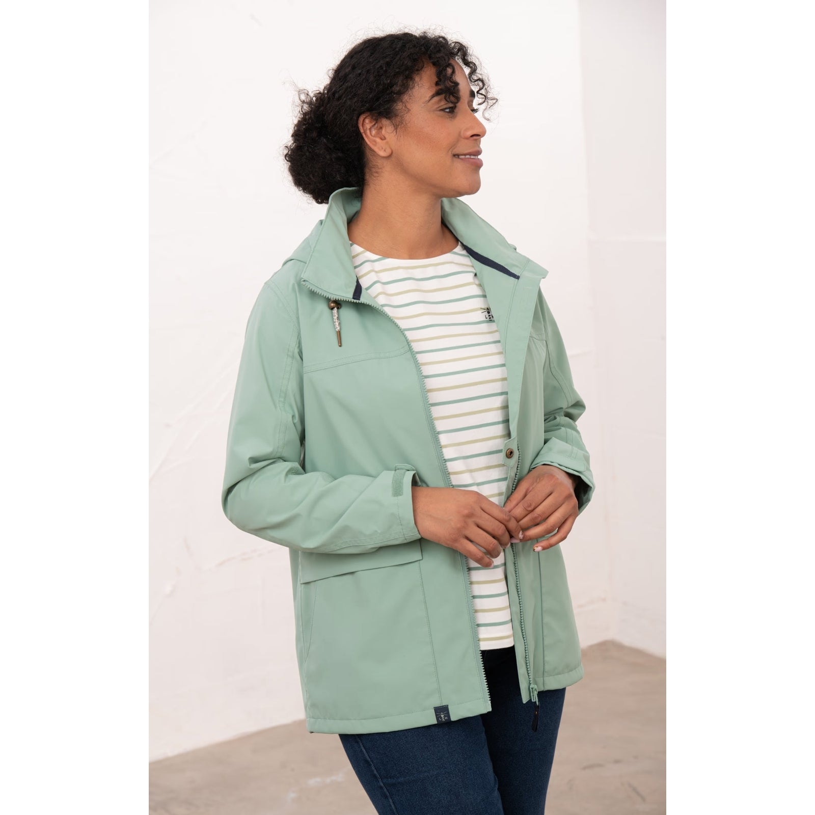 Side view of a woman wearing a Lighthouse waterproof Beachcomber II waterproof jacket in Basil green unzipped.