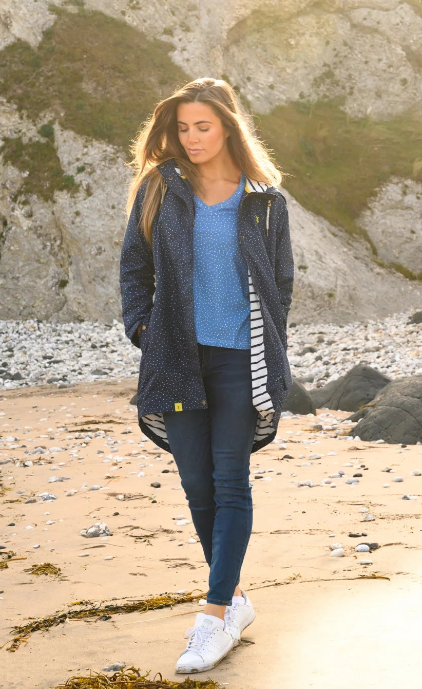 Lighthouse womens beachcomber jacket navy dot worn by woman walking on sandy beach with rocky background